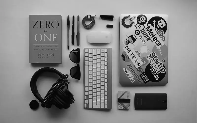Various tech devices such as a Laptop, keyboard, a computer mouse, headphones, and a book about learning to code